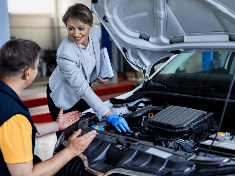 auto-mechanic-businesswoman-cooperating-while-checking-vehicle-hood-workshop